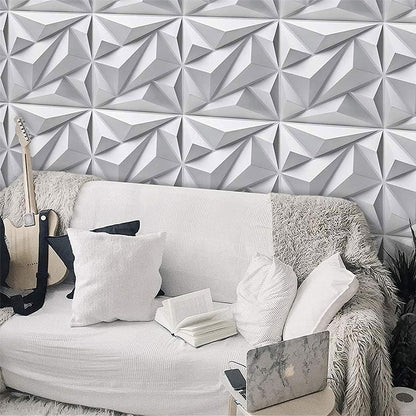 A living room with a white geometric accent wall, a white couch with throw pillows and a fluffy blanket, a laptop, an open book, and a guitar.