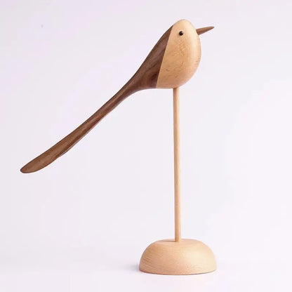 A single decorative wooden bird figurine with a long, sweeping tail, made from contrasting dark and light wood, standing on a tall, thin dowel and round base against a white background.