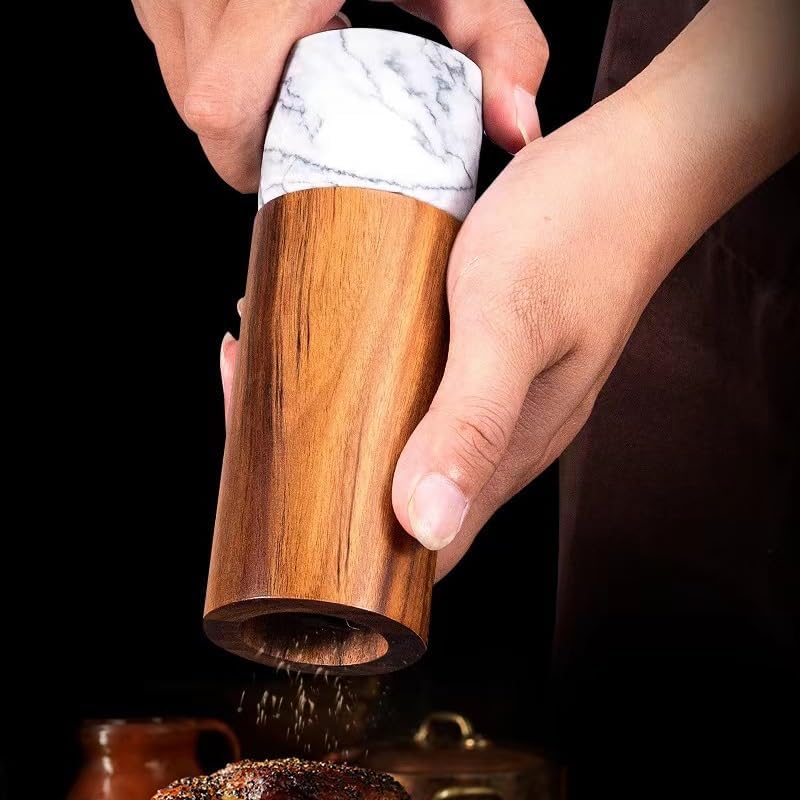 Wooden pepper grinder with marble top being used to sprinkle pepper on a dish.