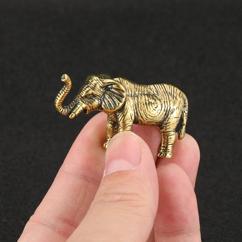A hand holds a small, gold-colored elephant figurine with its trunk raised.
