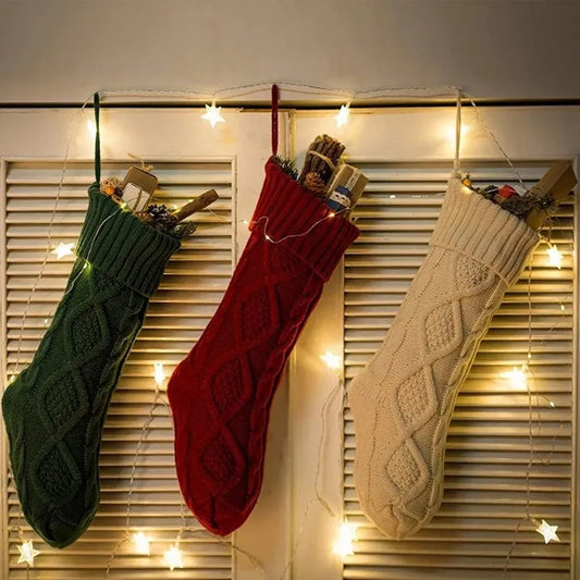Three knitted Christmas stockings filled with gifts, hanging with star lights.