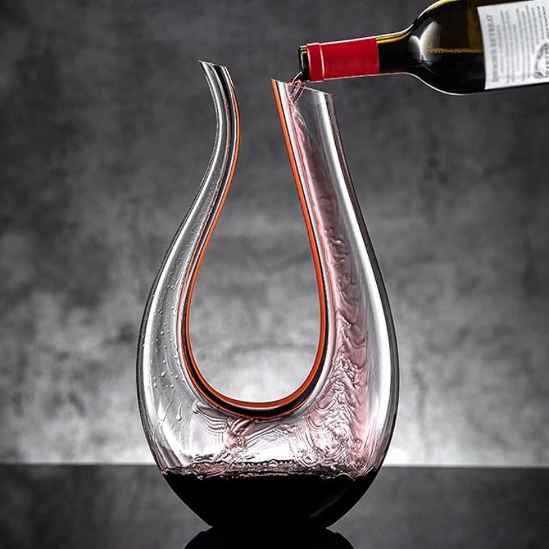 Glass wine decanter being filled with red wine from a bottle against a gray background