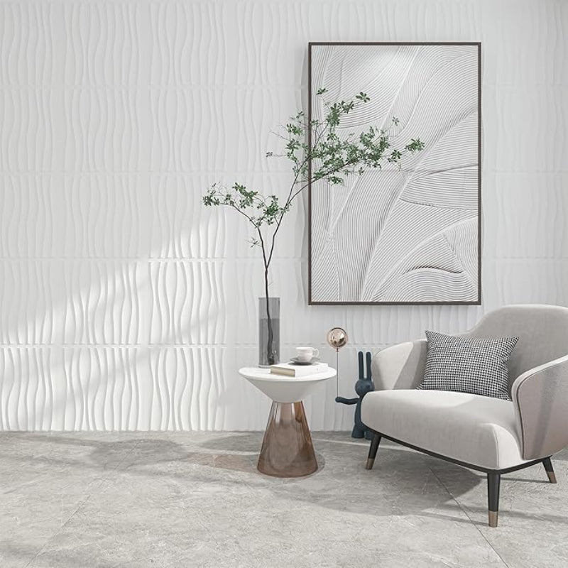 A modern room with a white wavy textured wall, a light grey armchair with a patterned pillow, a round side table with a plant, and abstract framed art.