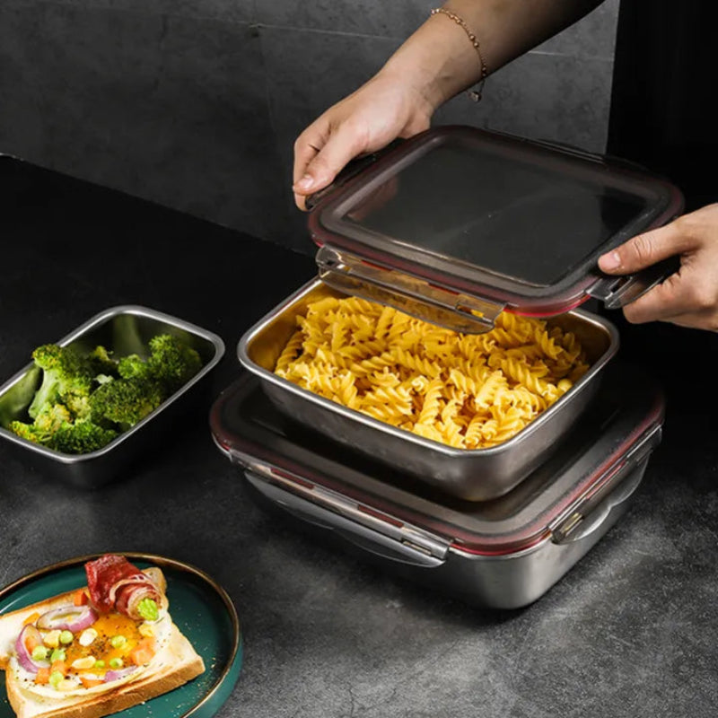 Hands place a lid on a stainless steel container filled with pasta, next to other food items.