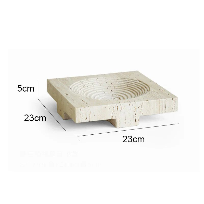 A square, beige travertine stone plate with a concentric circle pattern exudes natural beauty. Measuring 23cm wide and long, and 5cm high, it’s a subtle home styling piece elevated by a central base.