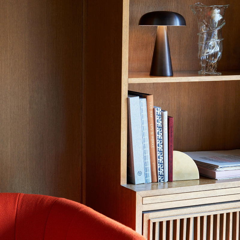 A black, mushroom-shaped lamp with a glowing light beneath its dome is styled on a wooden bookshelf.