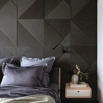 A modern bedroom features a bed with gray bedding and a light wood nightstand next to it, against a dark, geometric wood-paneled wall.