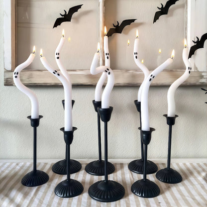 Halloween-themed candles with ghost faces on black stands against a neutral background.
