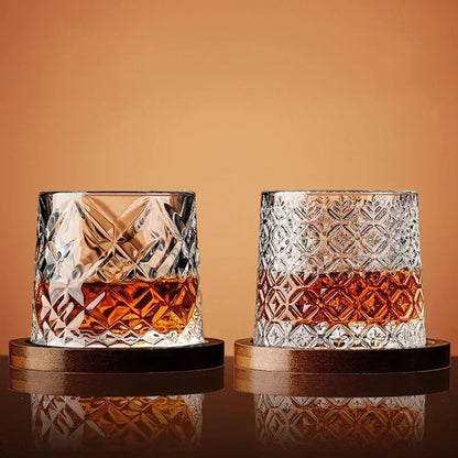 Two different styles of cut-crystal whiskey glasses, each filled with amber liquid and sitting on a wooden coaster.