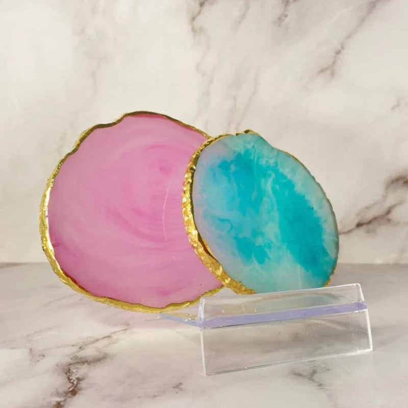 A set of two round agate coasters, each uniquely patterned with swirling earthy tones of pink and blue, placed on a marble counter.