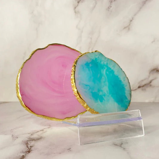 A set of two round agate coasters, each uniquely patterned with swirling earthy tones of pink and blue, placed on a marble counter.