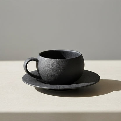 Textured matte black ceramic coffee cup and saucer set.