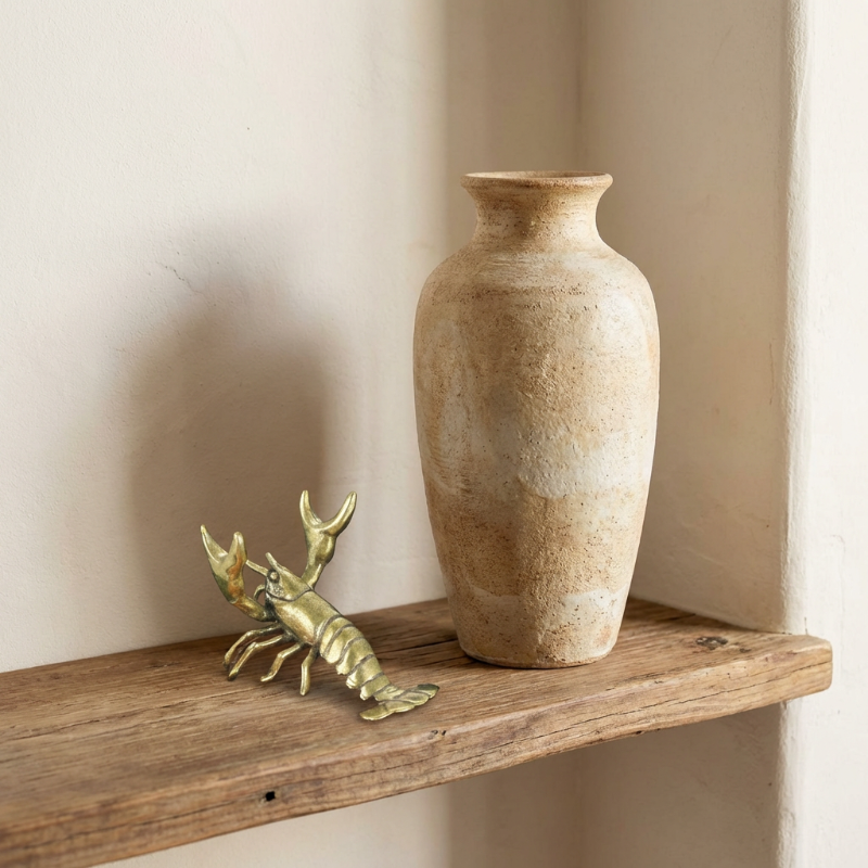 Vase and brass lobster figurine on a wooden shelf against a beige wall