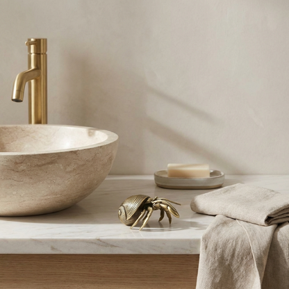 Bathroom sink with gold faucet, towel, and decorative shell on a neutral background