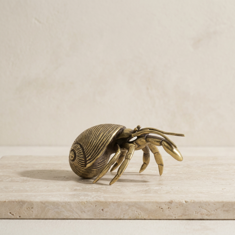Brass hermit crab sculpture on a light wooden surface with a beige background