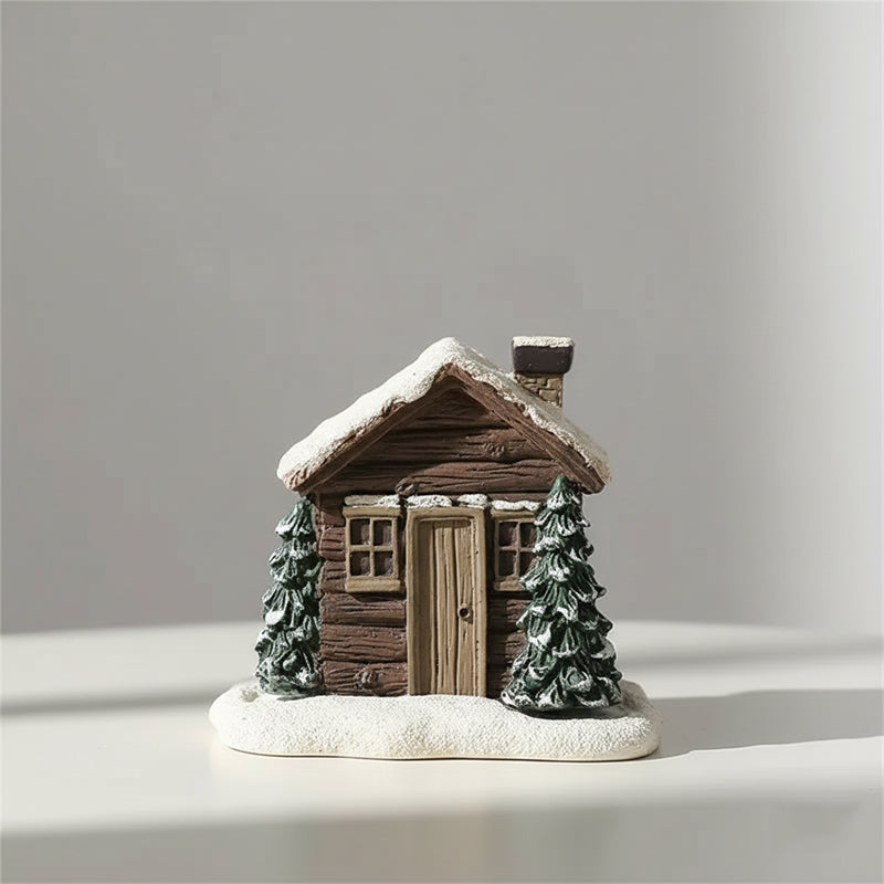Small model of a wooden cabin with snow on the roof, surrounded by trees, on a light gray background.