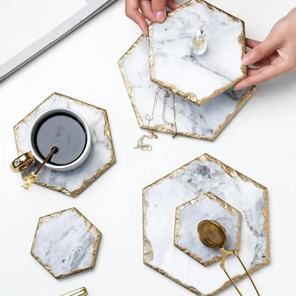 Hands placing a hexagon marble coaster on a table with other coasters, a cup of coffee, and a tea infuser.