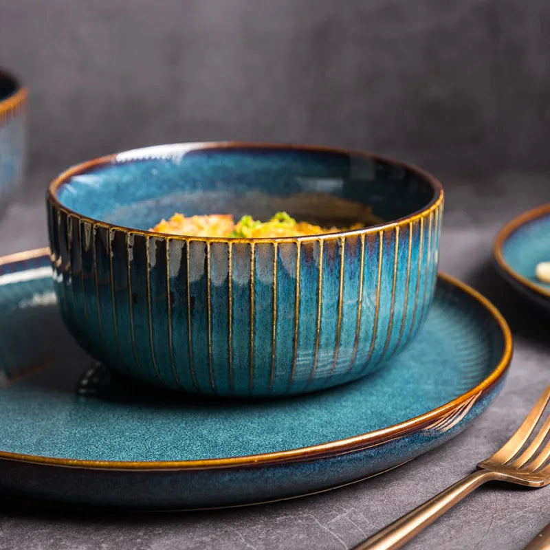 A deep blue ceramic bowl filled with food, sitting on a matching plate, with a golden fork.