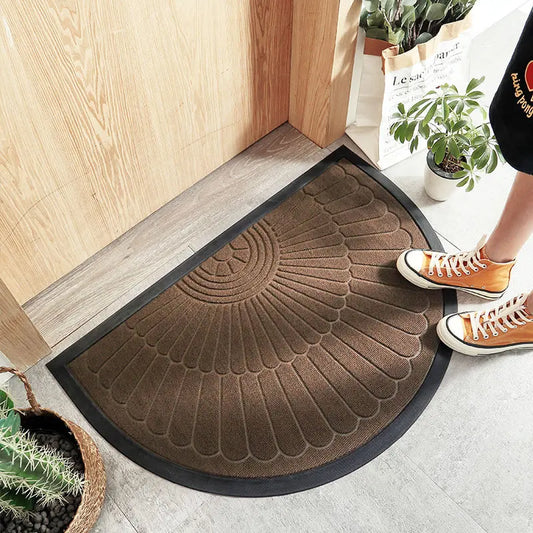 Brown half-circle welcome mat with a feather-like pattern in front of a wooden door.