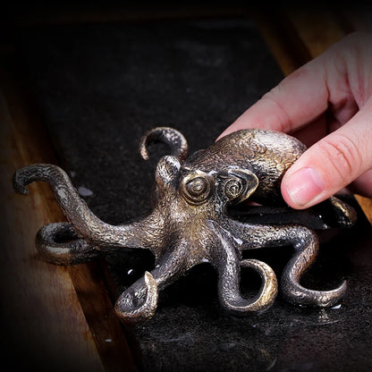 Bronze octopus sculpture held by a hand on a dark surface