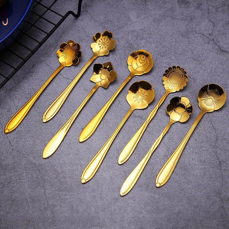 Eight golden flower spoons on a gray surface.