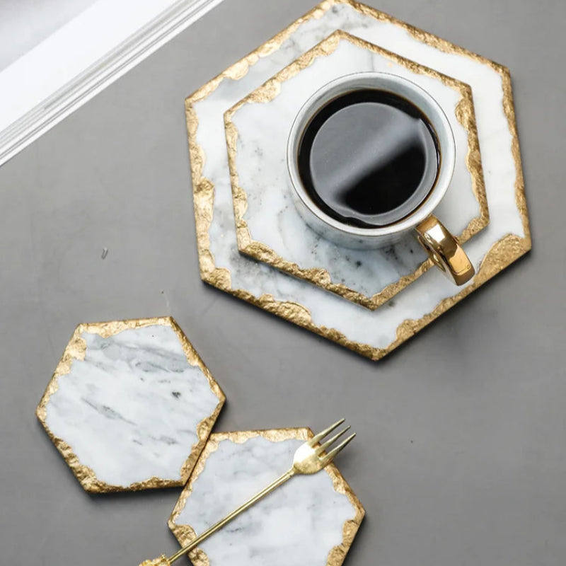 Coffee cup and gold fork on hexagonal marble and gold coasters.