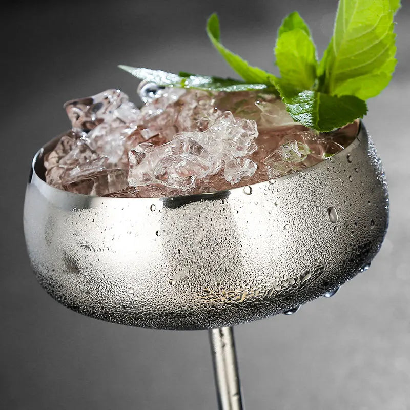 A sweating silver metal cocktail glass filled with crushed ice and mint leaves.