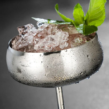 A sweating silver metal cocktail glass filled with crushed ice and mint leaves.