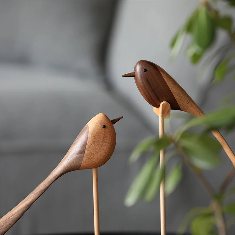 Close-up of two decorative wooden bird figurines, each made from two contrasting shades of wood, perched on thin wooden dowels.