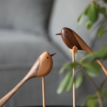 Close-up of two decorative wooden bird figurines, each made from two contrasting shades of wood, perched on thin wooden dowels.