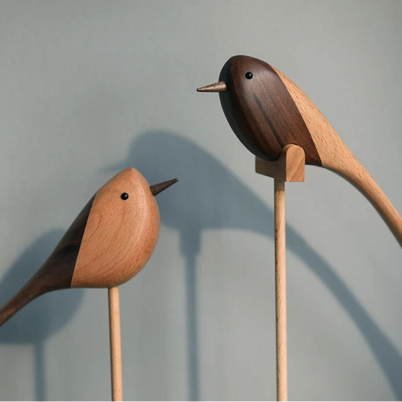 Close-up of two decorative wooden bird figurines, each made of contrasting light and dark wood, perched on thin wooden dowels.