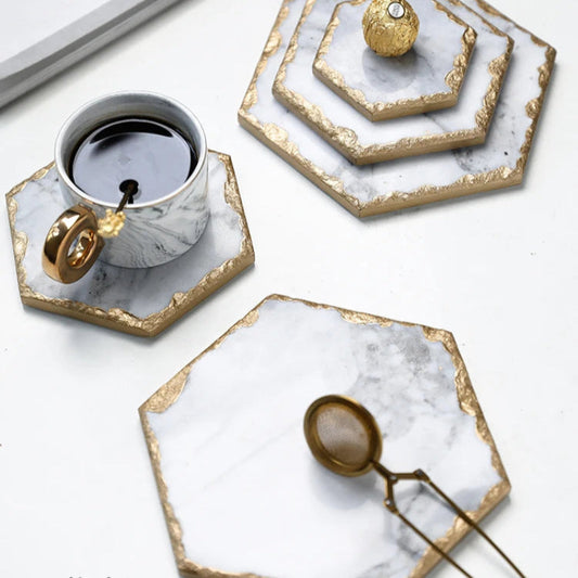 Coffee cup and gold tea infuser on marble and gold coasters.