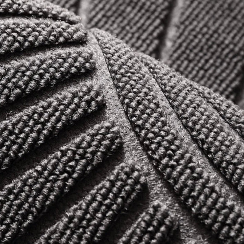 Close-up, high-angle shot of a grey, textured welcome mat with a raised geometric pattern.