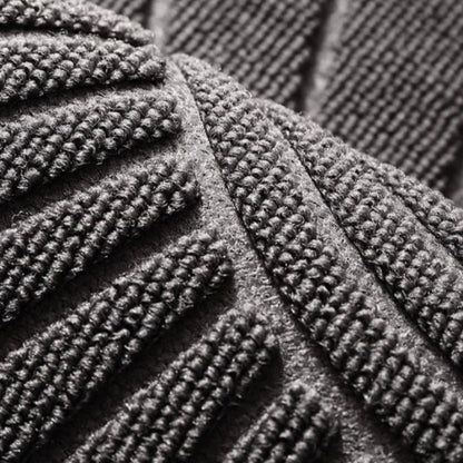 Close-up, high-angle shot of a grey, textured welcome mat with a raised geometric pattern.