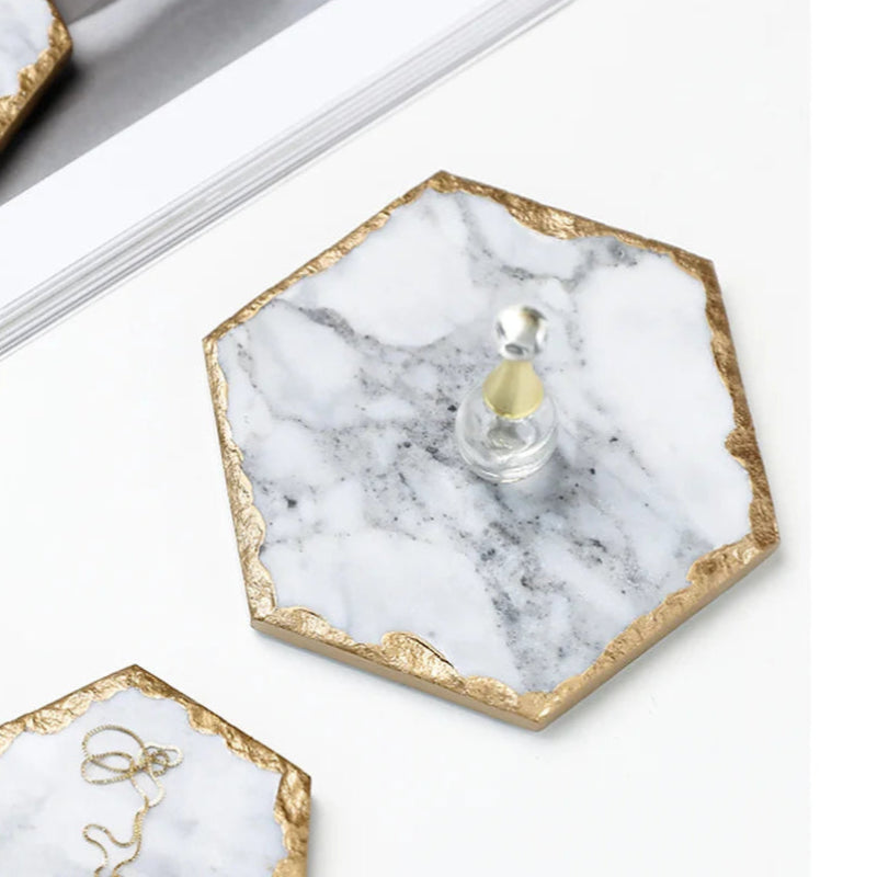 A hexagon-shaped coaster made of white marble with gold-painted edges.