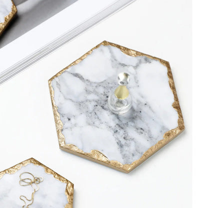 A hexagon-shaped coaster made of white marble with gold-painted edges.