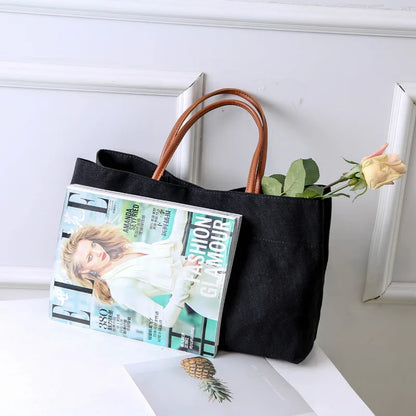 Black canvas tote bag with a magazine and flower.