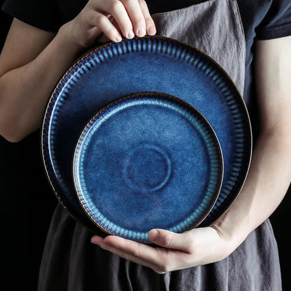 A person holds a pair of nested, deep blue ceramic plates with fluted edges.