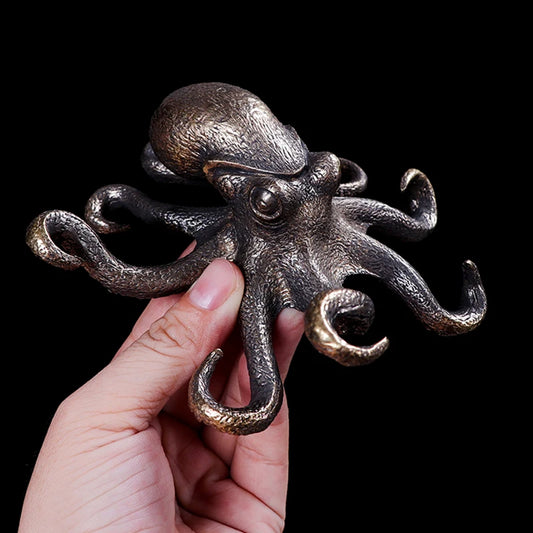 Metallic octopus sculpture held by a hand against a black background