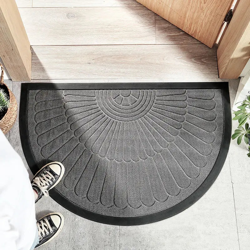 Black half-circle welcome mat with a feather-like pattern in front of a wooden door.