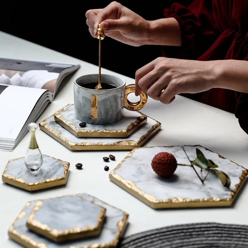 A person stirring coffee in a cup on a marble coaster, surrounded by more coasters, coffee beans, and a lychee fruit.