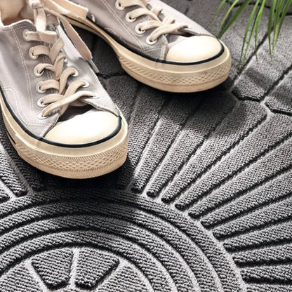 Close-up of light grey sneakers on a grey welcome mat with a ribbed fan-like pattern.