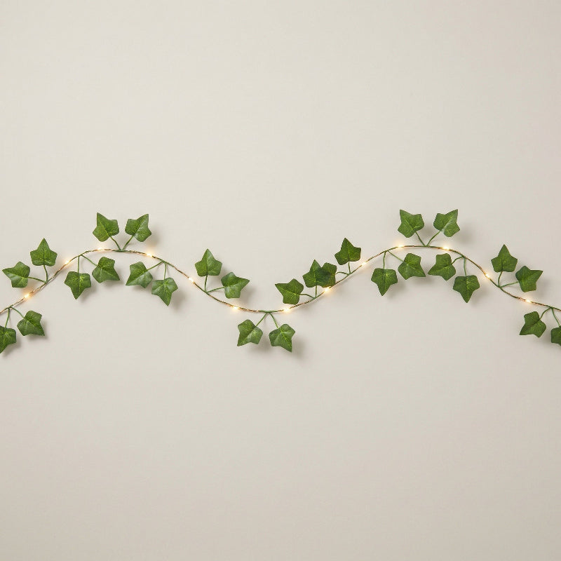 Decorative string lights with green leaf-like strands on a plain background