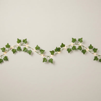 Decorative string lights with green leaf-like strands on a plain background