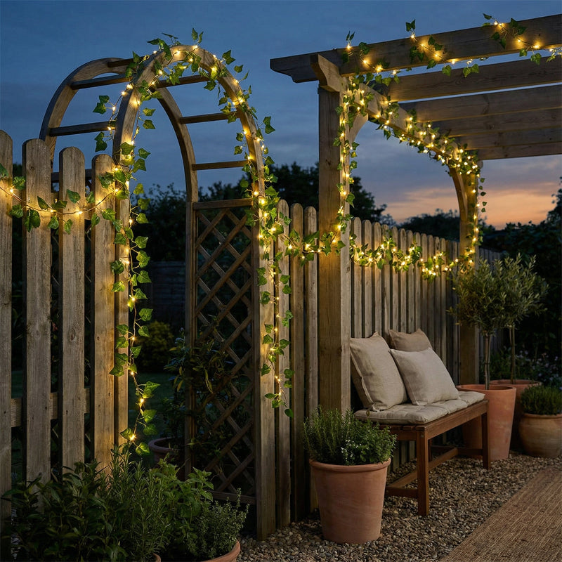 Garden setting with wooden arches and bench decorated with string lights and greenery.
