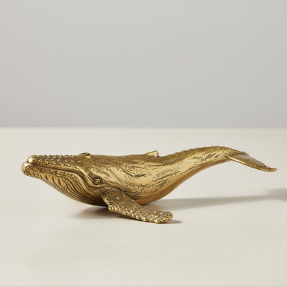 Gold whale figurine on a light beige surface with a neutral background