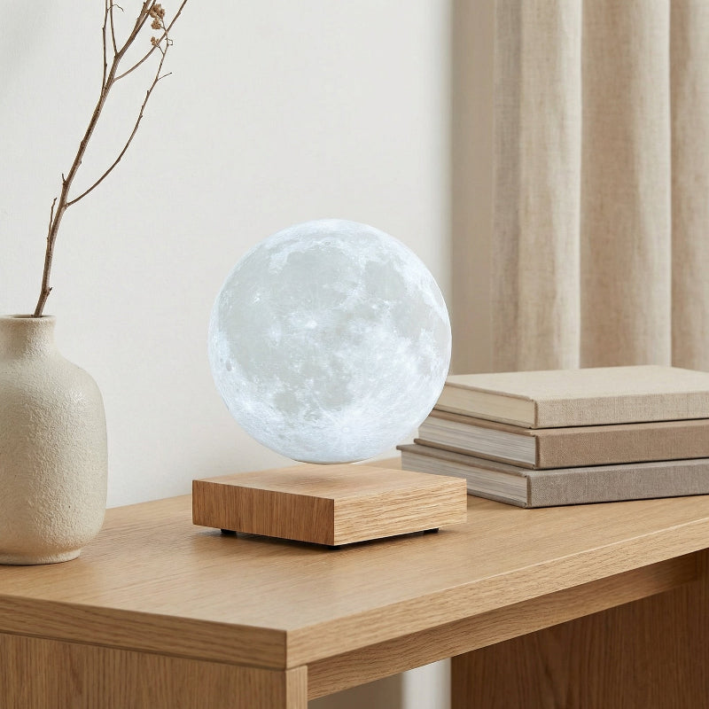 Moon lamp on a wooden surface with books and a vase in the background
