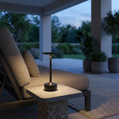 Outdoor setting with a table lamp on a stone table, surrounded by lounge chairs and plants.