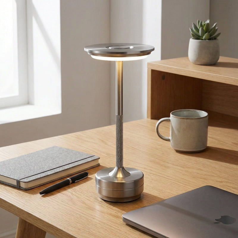 Modern desk setup with a lamp, notebook, pen, mug, and plant.