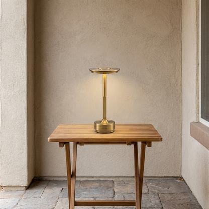 Gold outdoor lamp on a wooden table against a beige wall.